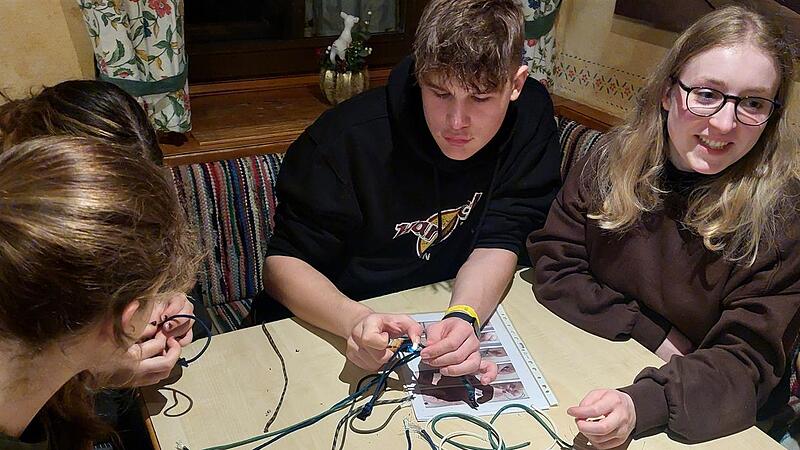 Jugendliche beim Abendprogramm auf der Foto Berghütte: Knüpfen von Paracord-Armbändern (Leander Martin aus Oberbach (Mitte) und Skicampleiterin Lysann Knopp aus Sailauf (rechts).