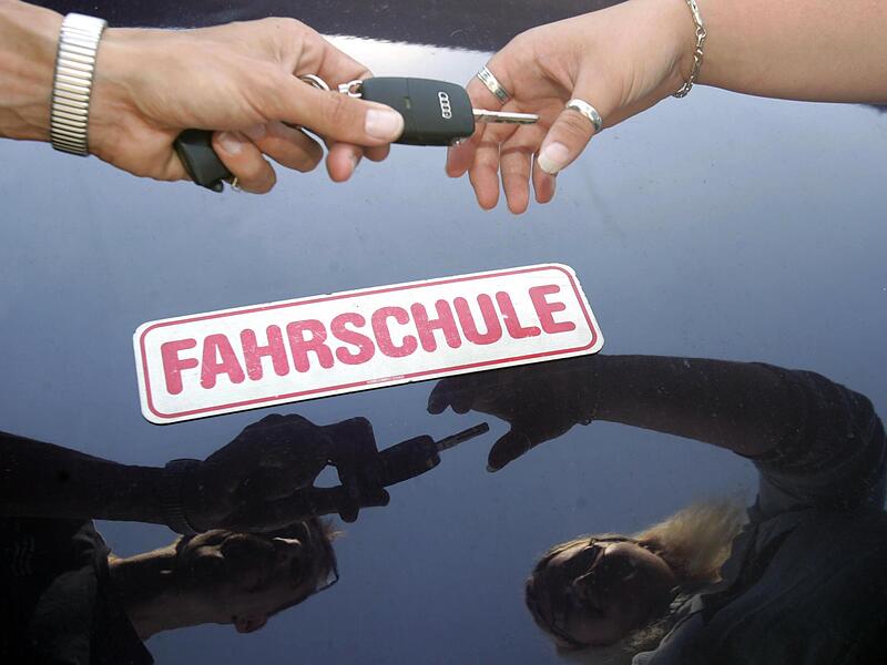 Ein Fahrlehrer überreicht seiner Fahrschülerin den Schlüssel zum Fahrzeug.