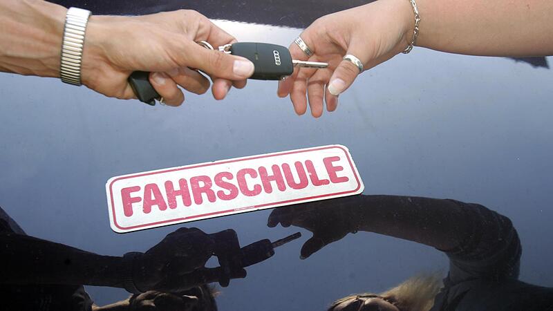 Ein Fahrlehrer überreicht seiner Fahrschülerin den Schlüssel zum Fahrzeug.