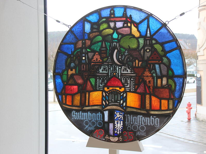 Einst hing dieses Fenster neben dem Eingang, jetzt schm&uuml;ckt es im Innenraum die Schaufenster. Das 1935 darin platzierte Hakenkreuz wurde nach dem Zweiten Weltkrieg durch die Stadtflagge ersetzt.