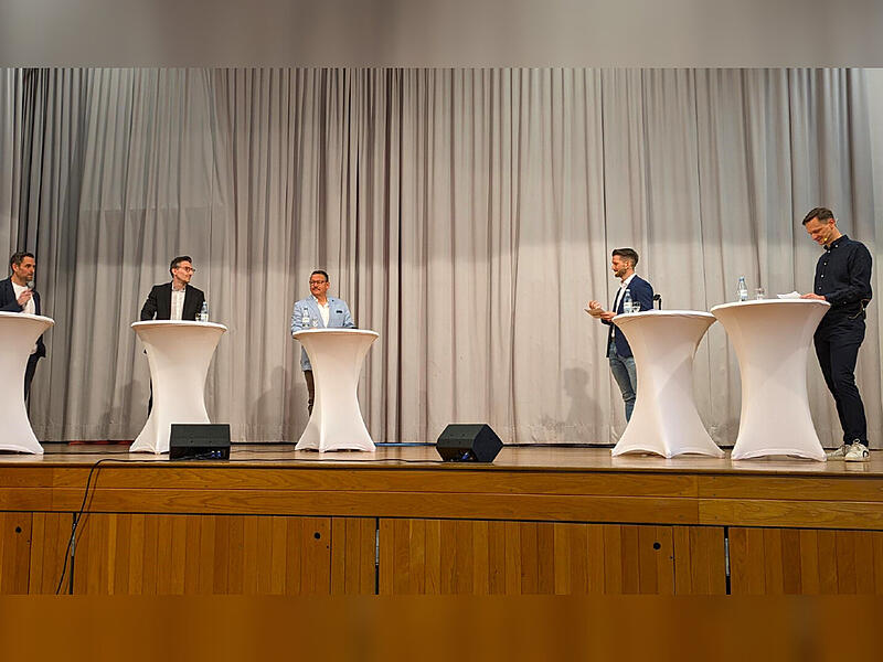 Das Podium läuft. Auf der Bühne stehen (v.l.) die Kandidaten Dirk Stumpe (PWG), Jan Marberg (SPD) und Heribert Übelacker (CSU), daneben Simon Snaschel (Mainpost) und Steffen Standke (Saale-Zeitung).