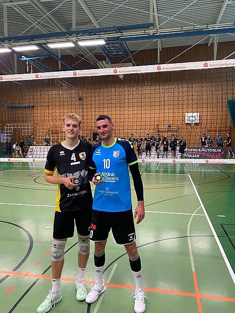 Zwei Herren stehen in einer Sporthalle und halten Medaillen.
