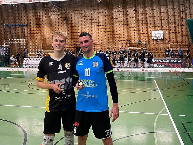Zwei Herren stehen in einer Sporthalle und halten Medaillen.