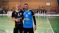 Zwei Herren stehen in einer Sporthalle und halten Medaillen.