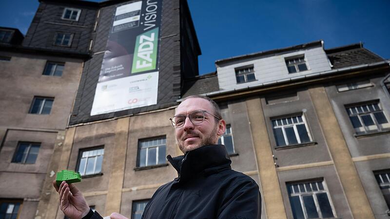 ohannes Zeck steht vor der Kirschbaumm&uuml;hle und und h&auml;lt zwei Modelle in der Hand. So wie das in Gr&uuml;n, k&ouml;nnte das Geb&auml;ude nach dem Umbau aussehen.