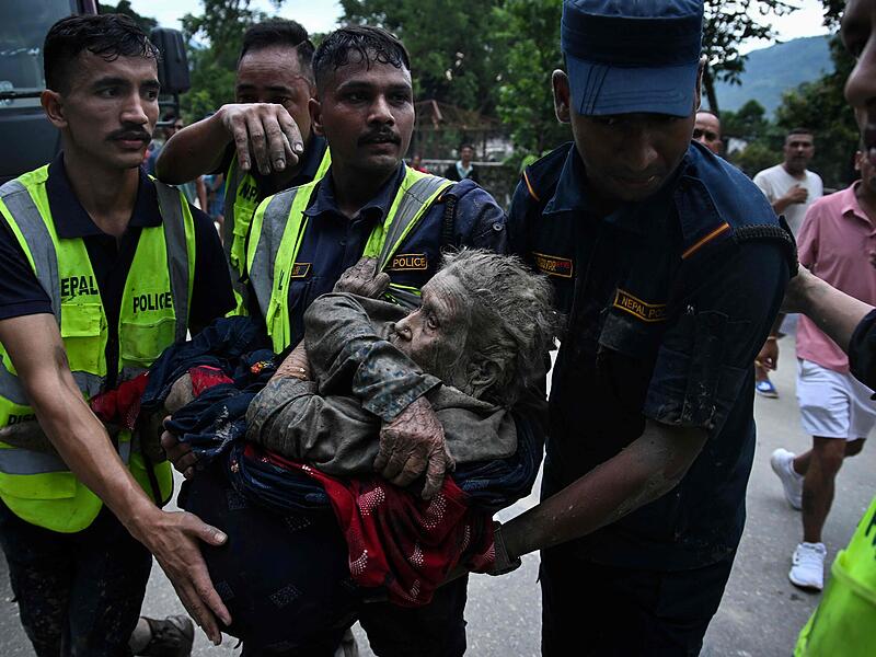 Rescuers carry in their arms a flood survivor, following flash floods and a landslide disaster in Devghat, in the Nepal's Nuwakot district on August 26, 2026. A massive flood and landslide disaster on the Nepal-Tibet border killed at least 103 people on August 26, 2026 and left several hundred missing, many of them foreign tourists. Aid workers said entire settlements had been "wiped out". Some 403 tourists -- 341 of them foreigners -- were unaccounted for several hours after the disaster struck, according to the tourism ministry. (Photo by PRAKASH MATHEMA / AFP)