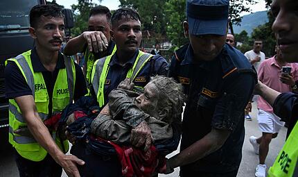 Rescuers carry in their arms a flood survivor, following flash floods and a landslide disaster in Devghat, in the Nepal's Nuwakot district on August 26, 2026. A massive flood and landslide disaster on the Nepal-Tibet border killed at least 103 people on August 26, 2026 and left several hundred missing, many of them foreign tourists. Aid workers said entire settlements had been "wiped out". Some 403 tourists -- 341 of them foreigners -- were unaccounted for several hours after the disaster struck, according to the tourism ministry. (Photo by PRAKASH MATHEMA / AFP)