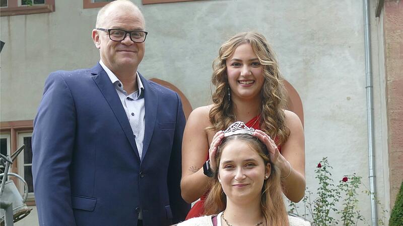 Der Vorsitzende des Weinbauvereins Achim Br&auml;unel steht den Weinhoheiten zur Seite als die bisherige Weinprinzessin Marla I. (hinten) die Krone ihrer Nachfolgerin Juliana I. aufs Haar setzt.