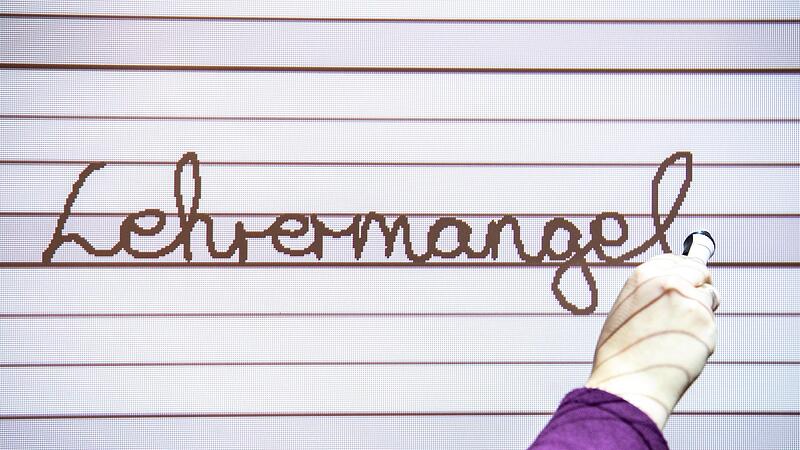 Eine Lehrerin schreibt auf ein Smartboard in einer Grundschule das Wort Lehrermangel. Eine Lehrerin schreibt auf ein Smartboard in einer Grundschule das Wort Lehrermangel.