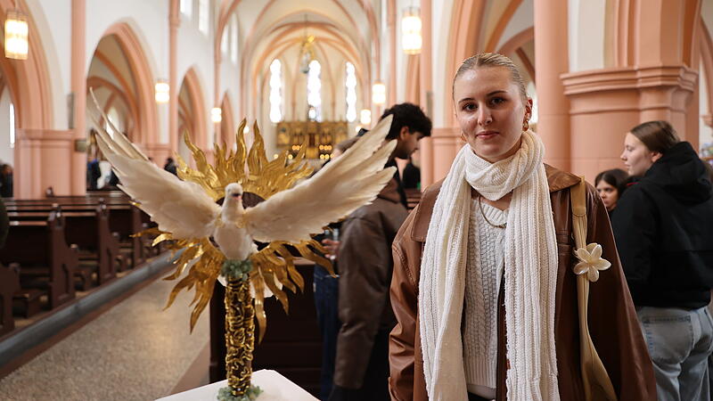 „Der trügerische Glanz“ nennt Annika Demmert ihr Werk. Eine weiße Taube, das universelle Friedenssymbol, steigt aus einem goldenen Kranz voller Flammen hervor: Doch die Kritik erschließt sich den Betrachtern von der anderen Seite. Denn in der Taube steckt ein Dolch in Kreuzform.