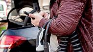 Ein Mann blickt an einer Lades&auml;ule auf ein Smartphone