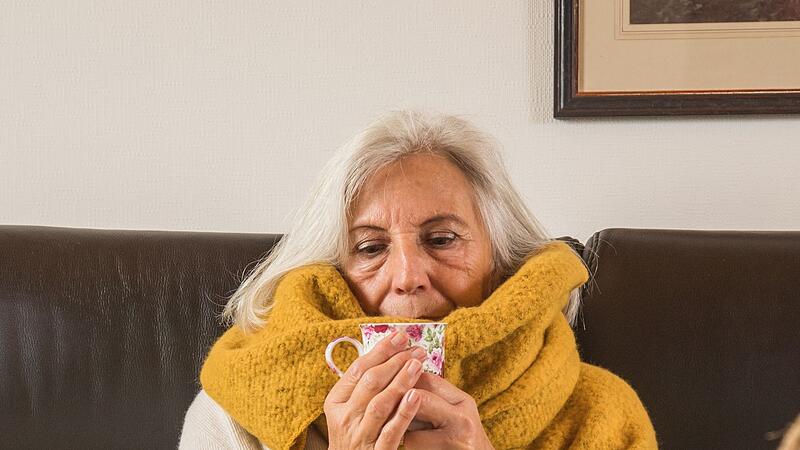 Eine Frau mit Erkältung trinkt Tee auf einem Sofa