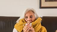 Eine Frau mit Erkältung trinkt Tee auf einem Sofa