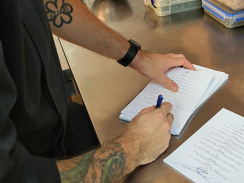 Dominik Käppeler unterschreibt die Menüs, die die Gäste erst am Ende des Abends erhalten. Auf dem linken Unterarm ist der Michelin-Stern als Tattoo zu sehen.