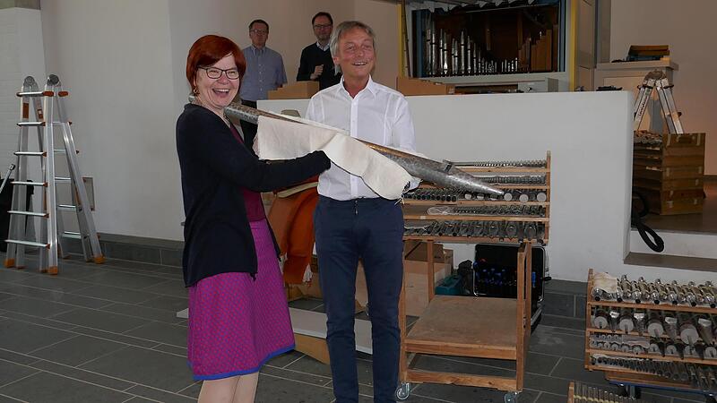 Pfarrer Oliver Schürrle aus Herzogenaurach übergibt eine Pfeife seiner Orgel an Pfarrerin Christiane Stahlmann von der Bubenreuther Lukasgemeinde, den künftigen Standort des Instruments. Seine Kirche bekommt eine neue Orgel.