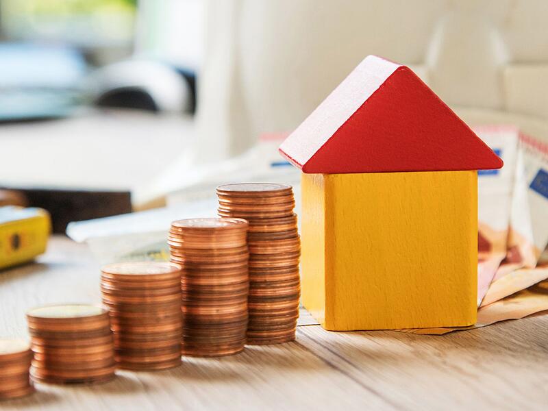 M&uuml;nzen und ein Haus aus Bausteinen liegen auf einem Tisch