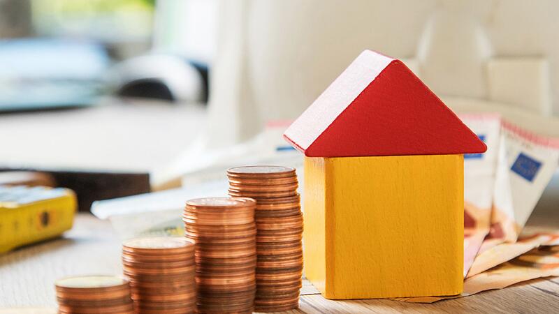 Münzen und ein Haus aus Bausteinen liegen auf einem Tisch Münzen und ein Haus aus Bausteinen liegen auf einem Tisch