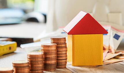 M&uuml;nzen und ein Haus aus Bausteinen liegen auf einem Tisch