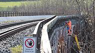 An der Bahnbrücke Euerdorf wird von Hubsteigern aus ein engmaschiges Drahtgewebe an den Randkappen angebracht, um lose Teile zu sichern. An der Bahnbrücke Euerdorf wird von Hubsteigern aus ein engmaschiges Drahtgewebe an den Randkappen angebracht, um lose Teile zu sichern.
