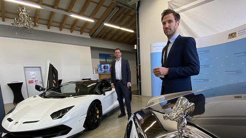 Der Bayerische Justizminister Georg Eisenreich (links) und Staatsanwalt Dr. Nino Goldbeck mit den beschlagnahmten Luxusschlitten, ein Rolls-Royce Phantom und ein Lamborghini Aventador.