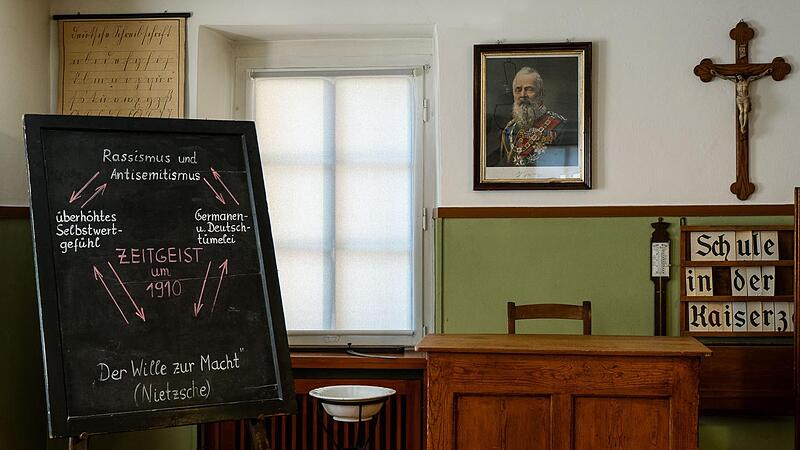 Das Klassenzimmer um 1910 weist auf den hierarchischen Aufbau hin: die Bänke auf unterster Ebene sind nach vorne ausgerichtet, erhöht auf einem Podest das Lehrerpult. Das zeigt den Ausdruck der Autorität des Lehrers als Vertreter der Staatsgewalt ...