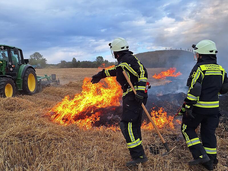 Ein Landwirt und zwei Feuerwehrkr&auml;fte versuchen,  einen Feldbrand bei Lautertal zu kontrollieren.