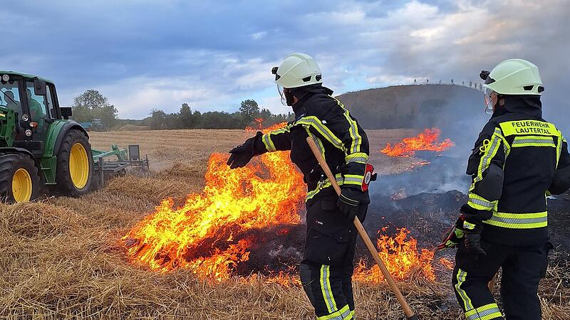 Ein Landwirt und zwei Feuerwehrkr&auml;fte versuchen,  einen Feldbrand bei Lautertal zu kontrollieren.