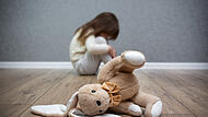 A stuffed bunny on the floor, a scared child sitting behind it. Child abuse. Bullying in the family. Symbolbild