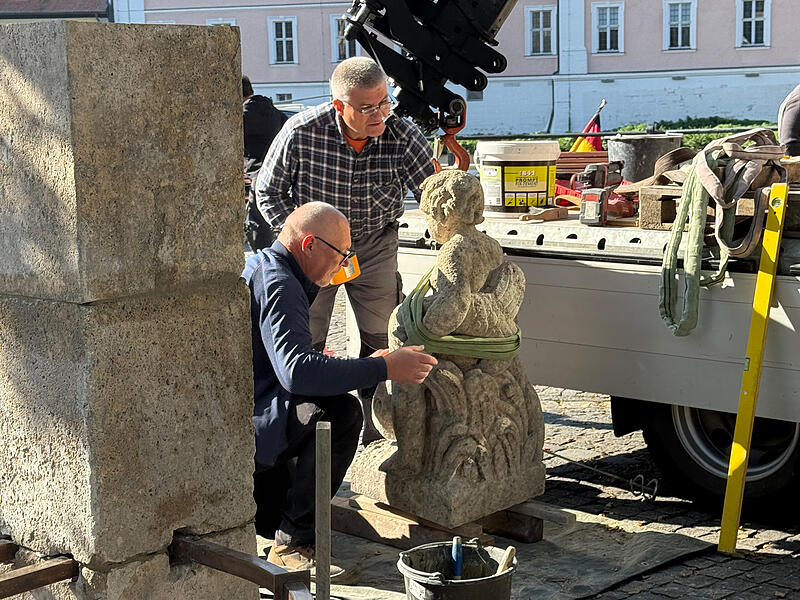 Steinmetz Konrad Götz (knieend) und sein Mitarbeiter montieren das Fischbrünnlein am Kranen.