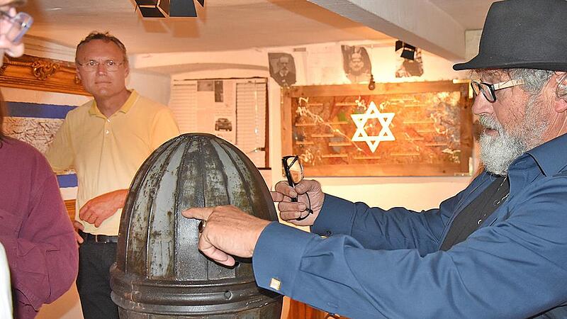 Der Künstler Hannes Betz erläutert den Gästen ein historisches Exponat seiner Ausstellung. Im Hintergrund ein Werk mit dem Davidstern als zentrales Symbol.