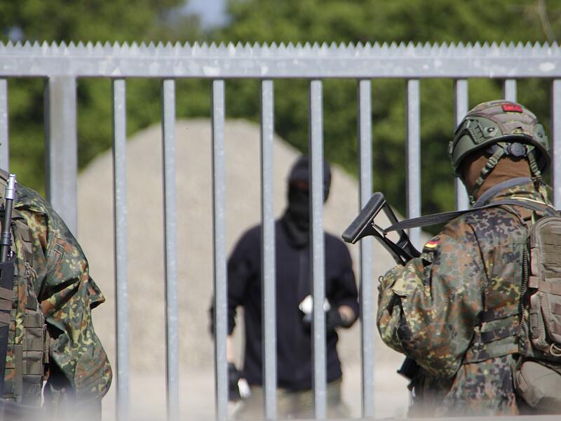 Die Zivilisten vor dem Tor werfen Steine und Stöcke auf die Soldaten der Bundeswehr. Die Zivilisten vor dem Tor werfen Steine und Stöcke auf die Kameraden der Bundeswehr.