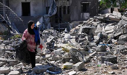 Aida Jleilati, die nach der Bekanntgabe einer vorl&auml;ufigen Waffenstillstandsvereinbarung zwischen den Vereinigten Staaten und dem Iran in ihr Dorf zur&uuml;ckgekehrt ist, tr&auml;gt ihre Habseligkeiten &uuml;ber die Tr&uuml;mmer ihres zerst&ouml;rten Hauses.