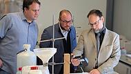 Sebastian Kamps (von rechts), Geschäftsführer von TC-Tungsten Compounds, zeigt Landrat Sebastian Sraubel (CSU) und Andre' Dehler, den zweiten Bürgermeister der Gemeinde Grub am Forst, wie man die Dichte einer Schwerflüssigkeit misst.