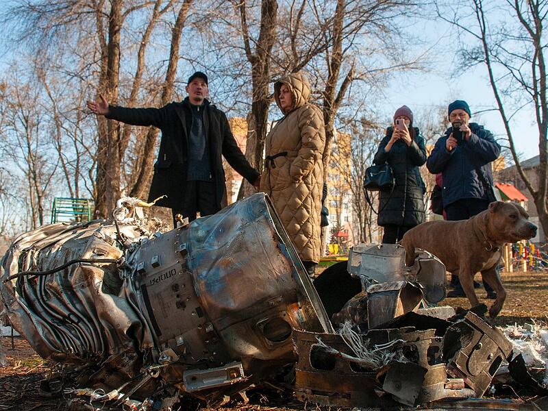 Menschen stehen neben Fragmenten eines Flugkörpers auf der Straße nach einem offensichtlichen russischen Angriff. Die russischen Truppen haben ihren erwarteten Angriff auf die Ukraine gestartet.