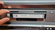 Johannes Michel legt die VHS-Kassette, die unter anderem eine Aufnahme seiner Erstkommunion enthält, in den Videorekorder ein. Darunter steht der Festplattenrekorder, auf den der Inhalt der VHS dann übertragen wird.