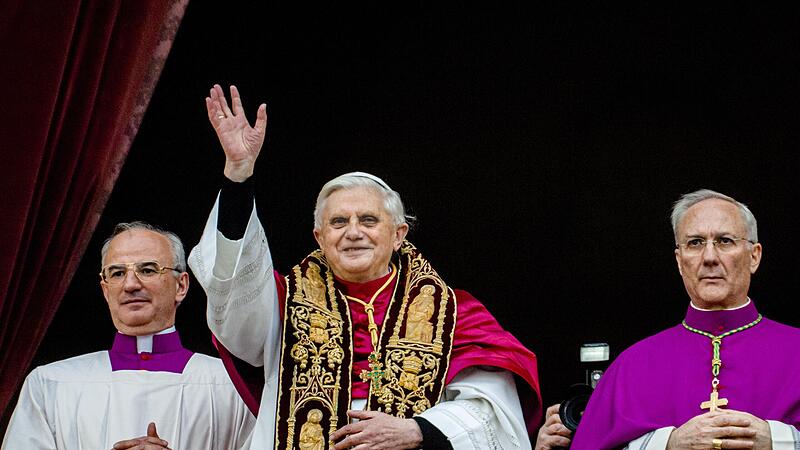 Joseph Ratzinger grüßt kurz nach seiner Wahl zum Oberhaupt der katholischen Kirche im April 2005 vom zentralen Balkon des Petersdoms die Menge. Neben ihm stehen Monsignore Francesco Camaldo (links) und Bischof Piero Marini.