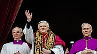 Joseph Ratzinger grüßt kurz nach seiner Wahl zum Oberhaupt der katholischen Kirche im April 2005 vom zentralen Balkon des Petersdoms die Menge. Neben ihm stehen Monsignore Francesco Camaldo (links) und Bischof Piero Marini.