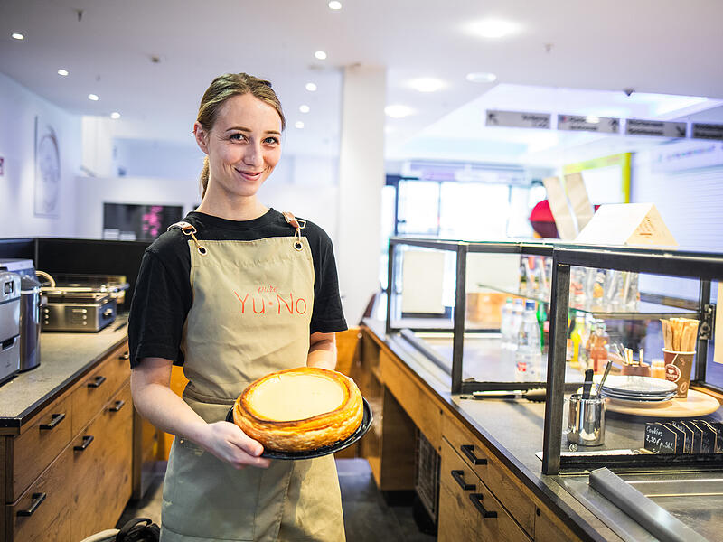 Café Yu No Mitarbeiterin Solène Perron präsentiert einen der glutenfreien Kuchen, die im Café Yu No im Ertl-Zentrum in Hallstadt angeboten werden.