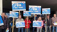 Mit Plakaten, auf den sie die Wiedereinführung der 10-H-Regelung fordern, haben Mitglieder der Bürgerinitiative das Prokon-Team begrüßt.