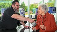 Andreas Rösch, Veranstaltungstechniker bei Bamberg Congress Event, und Margit Gamberoni von der Selbsthilfegruppe OhrRing für Schwerhörige und Cochlea-Implantat-Träger erklären, wie die Induktionsschleife richtig benutzt wird.