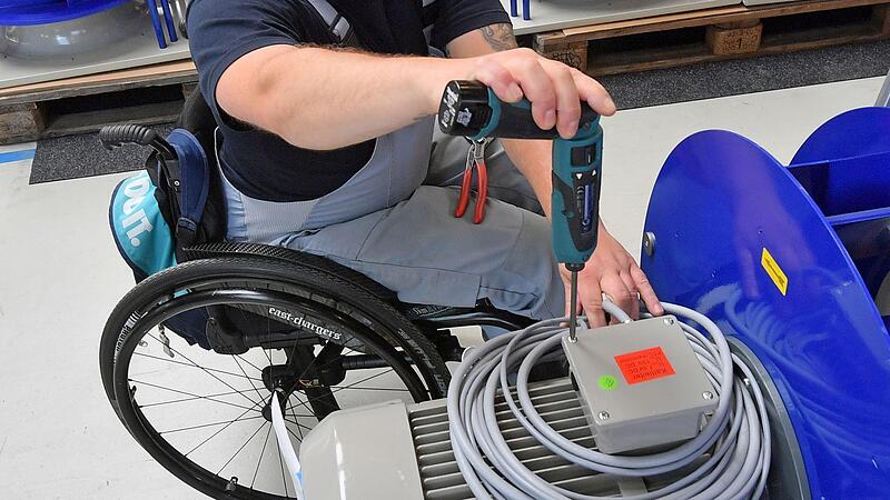 An einem Arbeitsplatz ist ein behinderter Mitarbeiter im Rollstuhl mit Montagearbeiten besch&auml;ftigt.