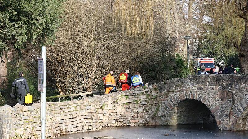 Rettungskräfte und Kriminaltechniker gehen in der Nähe des Tatortes eine kleine Brücke hinauf.