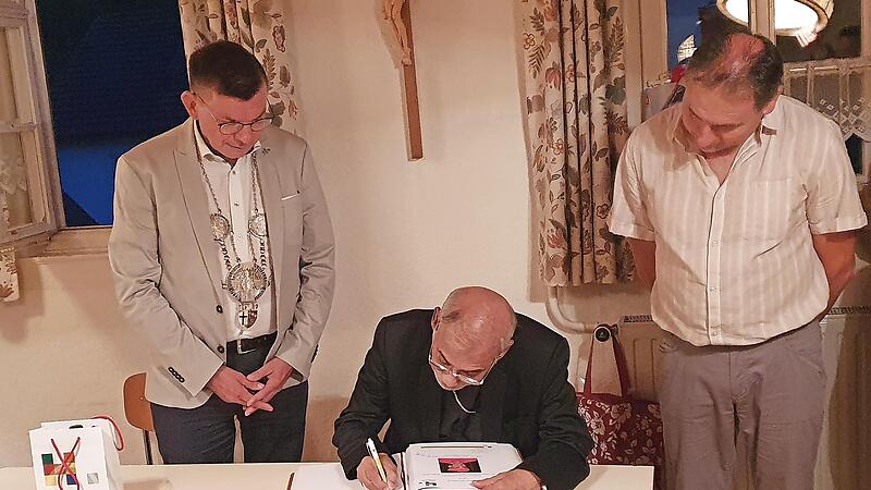 B&uuml;rgermeister Armin Warmuth (links) holte beim zweiten Besuch des Kardinals die Eintragung in das goldene Buch der Stadt Hammelburg nach. Rechts: Ortsbeauftragter Bernd H&uuml;fner.