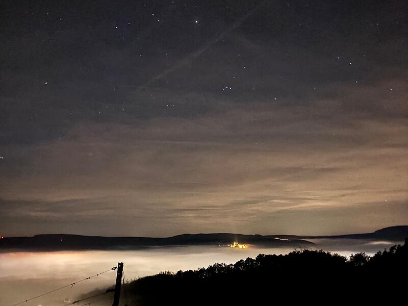 Einen faszinierenden Blick hatte Joshua Koch aus Machtilshausen als er mit Freunden am terroir-f am Ofenthaler Berg oberhalb von Hammelburg unterwegs war. W&auml;hrend man von Hammelburg nur noch die im Nebel des Saaletals versinkenden Lichter erkennen kann, leuchtet Schloss Saaleck im Hintergrund unter dem Sternenhimmel.