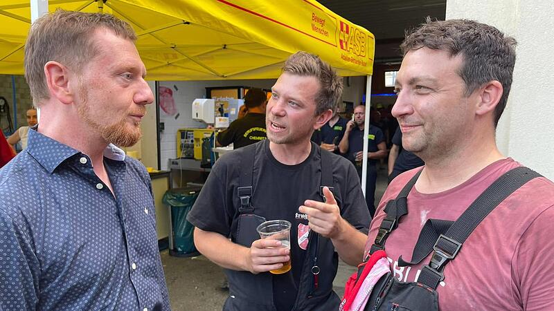 Der Gößweinsteiner Feuerwehrkommandant Marcel Zweck (M.) und der Gößweinsteiner Feuerwehrmann Thomas Pensel (r.) sprechen in Bad Schandau mit Sachsens Ministerpräsident Michael Kretschmer.Forchheim & Fränkische Schweiz