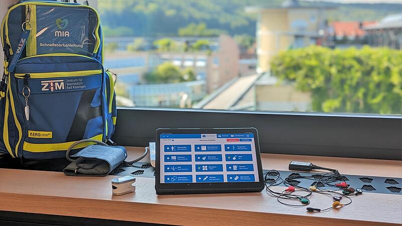 Auf dem Tablet ist die Oberfl&auml;che der App Mia zu sehen. Im nebenstehenden Rucksack befinden sich die Ger&auml;te, die MFAs beim Hausbesuch ben&ouml;tigen. Moderne Ger&auml;te lassen sich via Bluetooth mit dem Tablet verbinden.