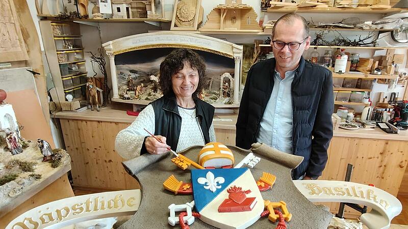 Lisa Schinner (hier mit Pfarrer Pater Florian) stellt mit letzten Pinselstrichen das neue Wappenschild von Papst Leo XIV. für die Basilika Marienweiher fertig.