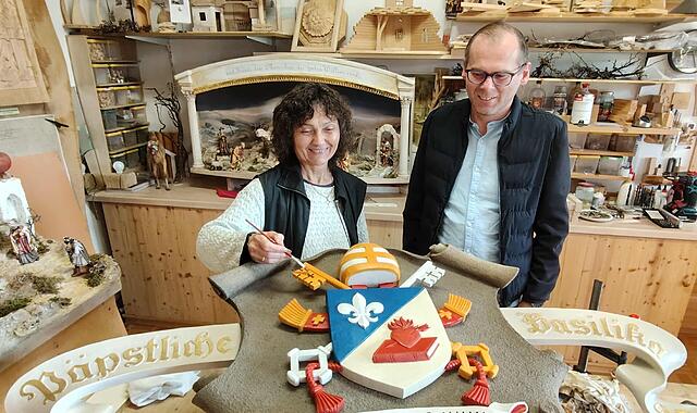 Lisa Schinner (hier mit Pfarrer Pater Florian) stellt mit letzten Pinselstrichen das neue Wappenschild von Papst Leo XIV. für die Basilika Marienweiher fertig.