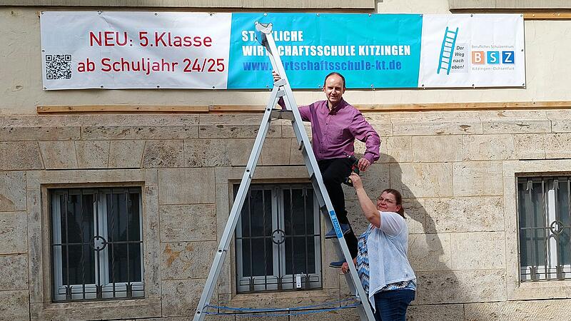 Steffen Prepens und Bettina Schütz machen mit einem großen Banner auf das neue Angebot aufmerksam: Die staatliche Wirtschaftsschule Kitzingen kann nun ab der 5. Klasse besucht werden.