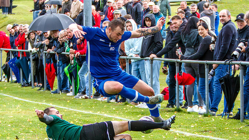 Der  Mainleuser  Kapitän Manuel Wollner grätscht an der Außenlinie vor zahlreichen Zuschauern Maximilian Weiß von der SG Oberland den Ball weg.